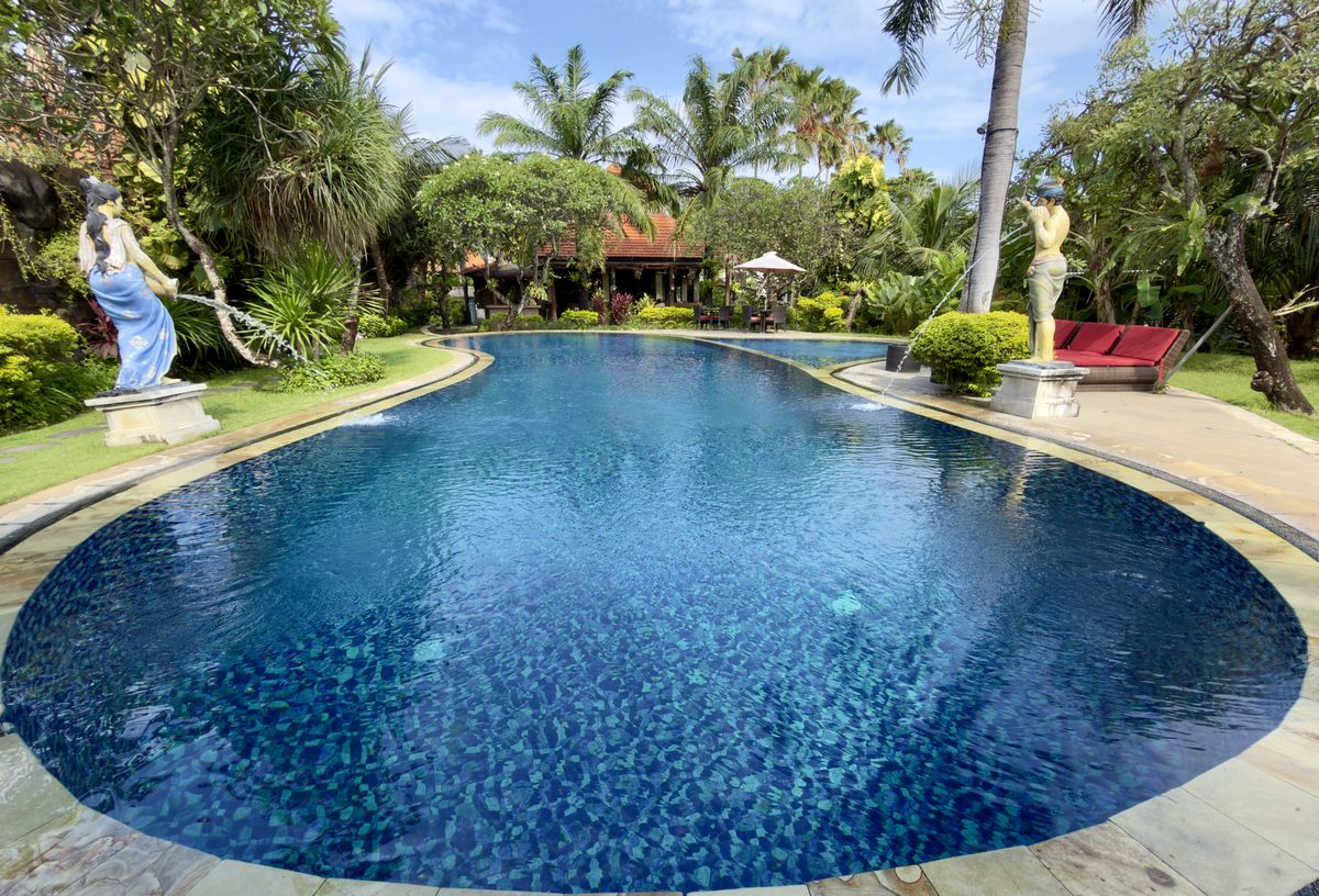 Curved blue resort pool with tropical garden and sun lounges